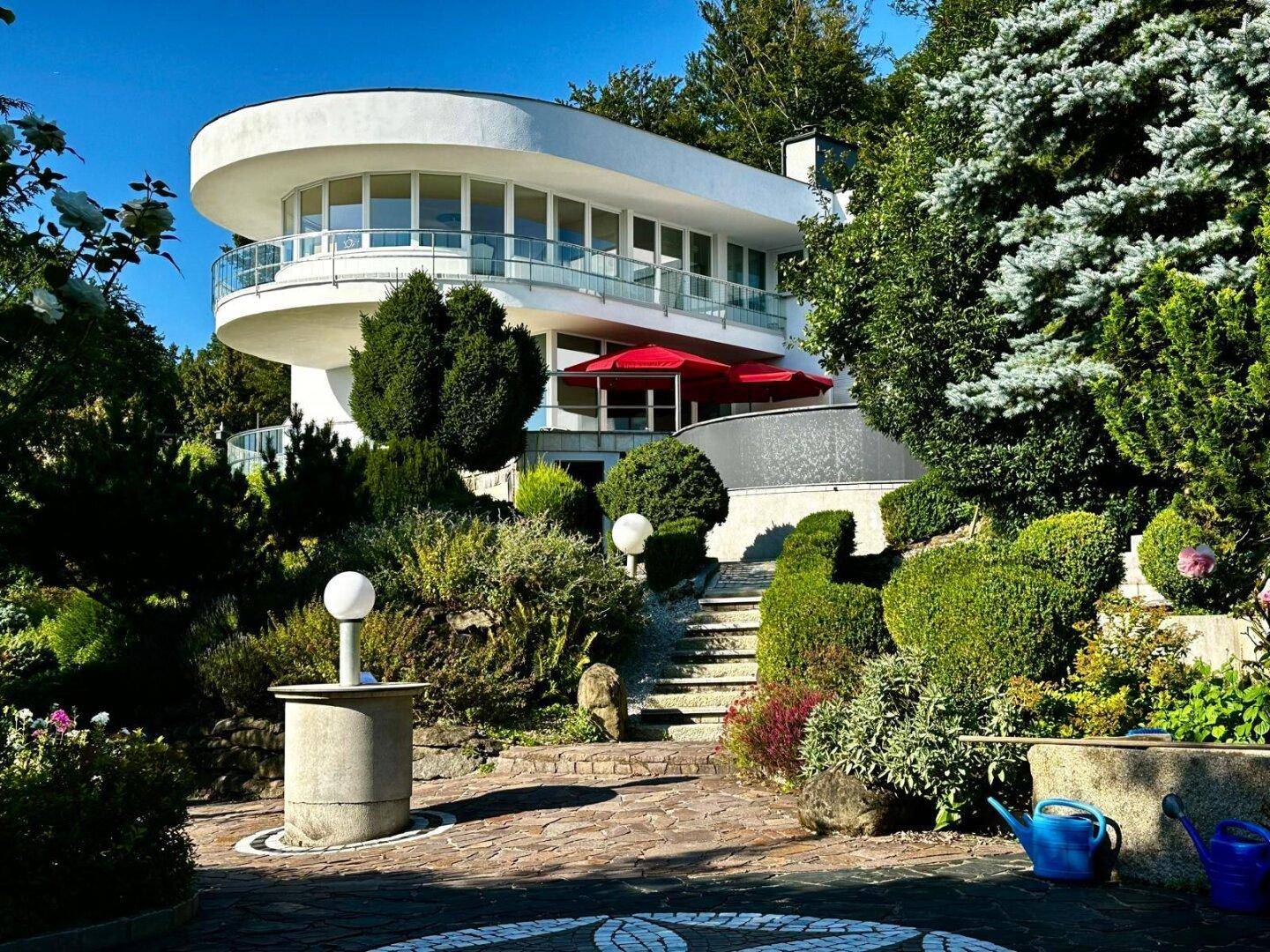 Elegantes modernes Haus umgeben von einem üppigen, terrassierten Garten mit vielfältiger Bepflanzung.