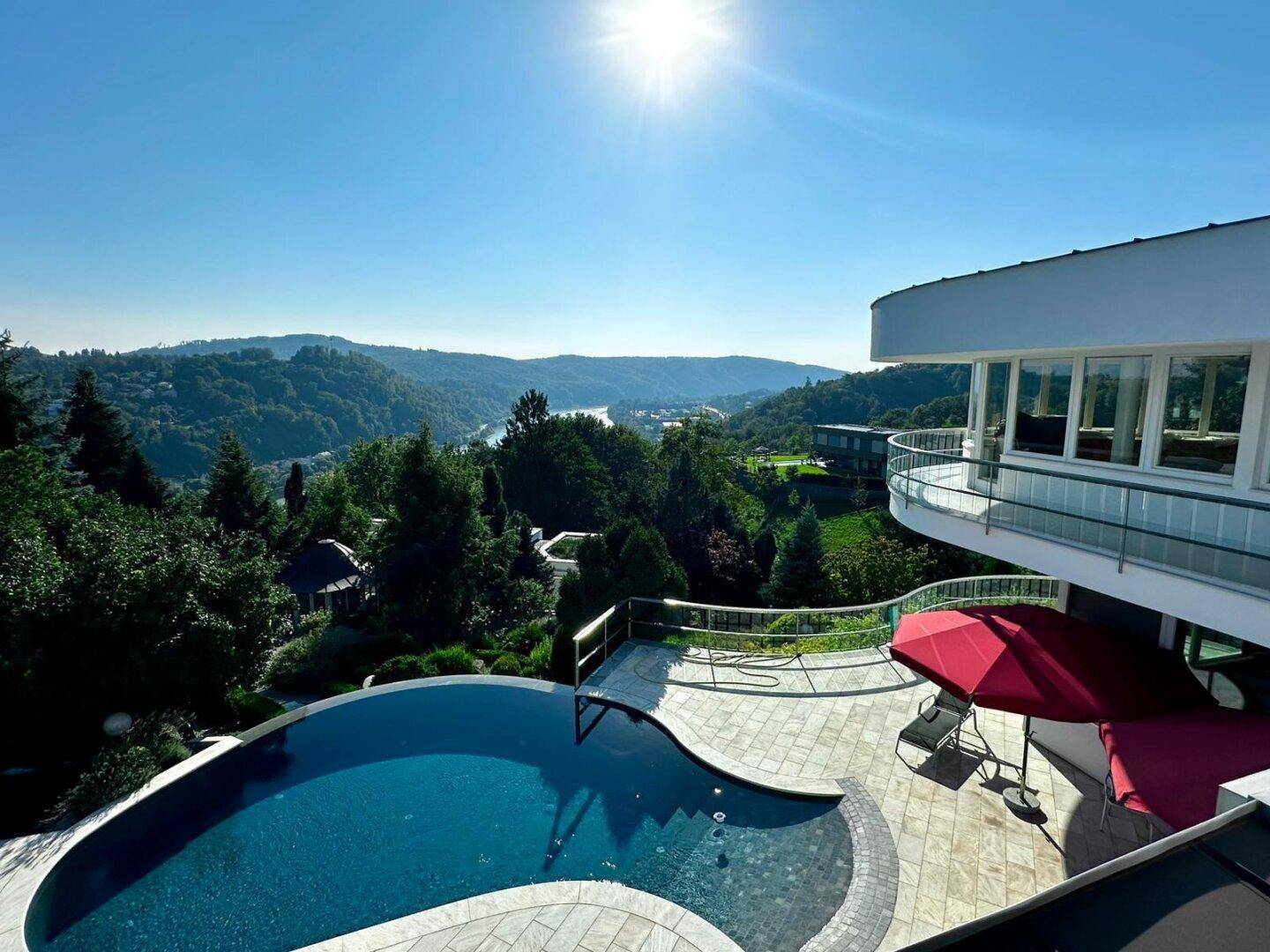 Panoramablick auf das moderne Anwesen mit geschwungenem Pool und weitreichender Aussicht auf die grüne Landschaft.