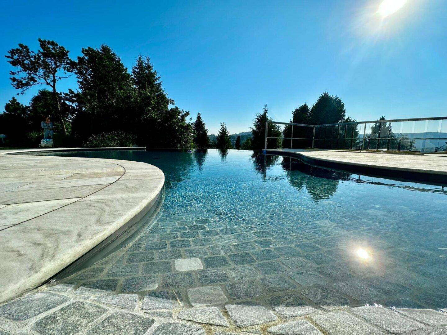 Detailaufnahme des eleganten Pools mit flachem Einstieg und spiegelnder Wasseroberfläche unter blauem Himmel.