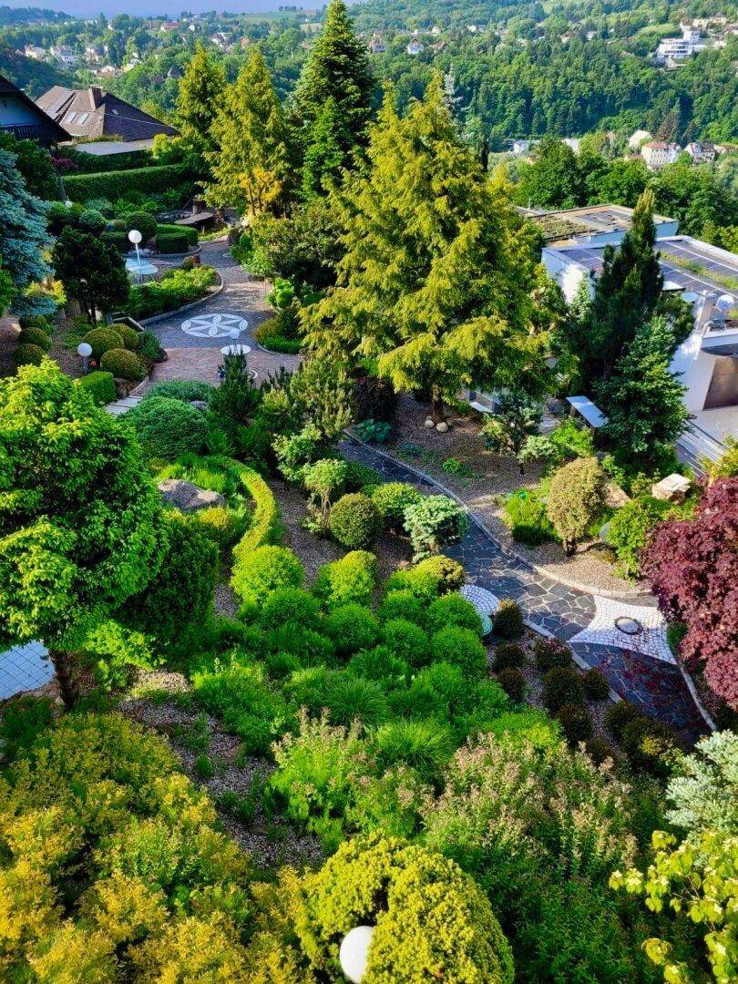 Weitläufiger, terrassierter Garten mit kunstvoll angelegten Wegen, vielfältiger Bepflanzung und altem Baumbestand.