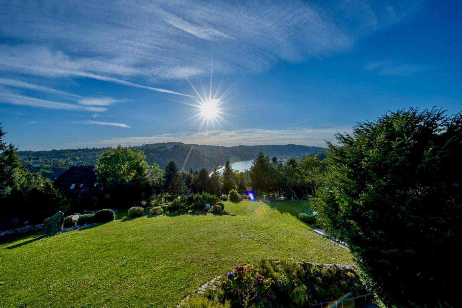 Große Rasenfläche im Garten mit weitem Blick auf die hügelige Landschaft und einen See in der Ferne.