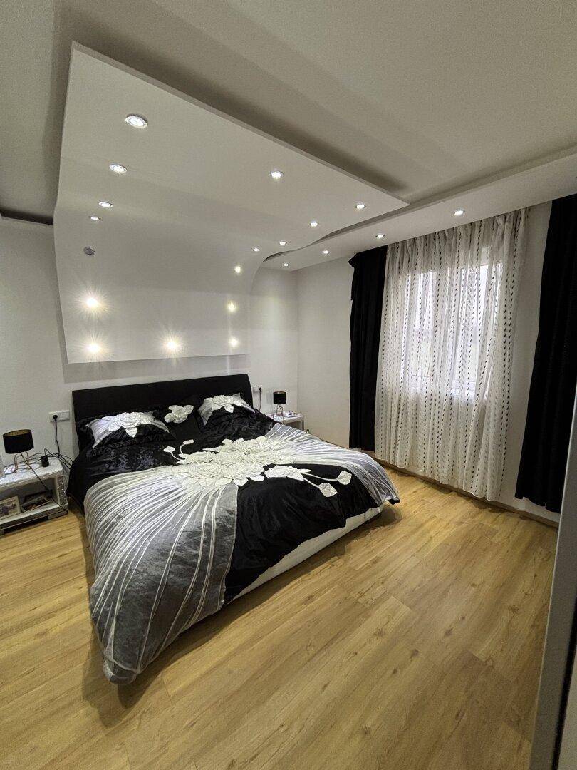 Modernes Schlafzimmer mit großem Doppelbett, Holzfußboden und indirekter Deckenbeleuchtung.