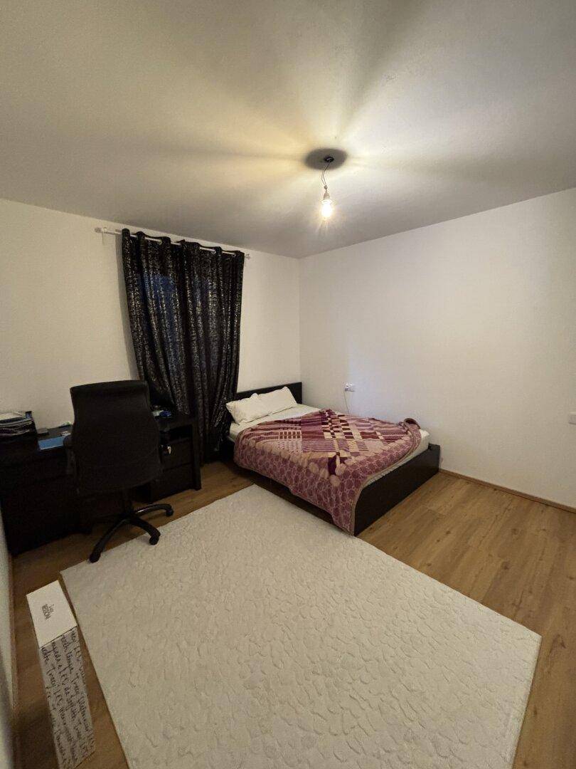 Einfaches Schlafzimmer mit Einzelbett, Schreibtisch und Holzfußboden.