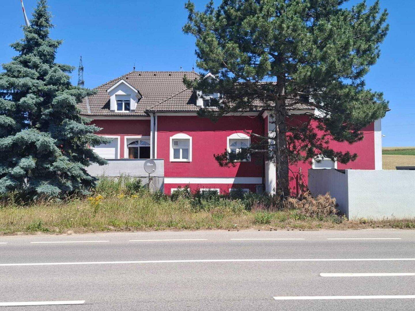 Ansicht des roten Gebäudes mit weißer Fassade und Bäumen unter blauem Himmel.