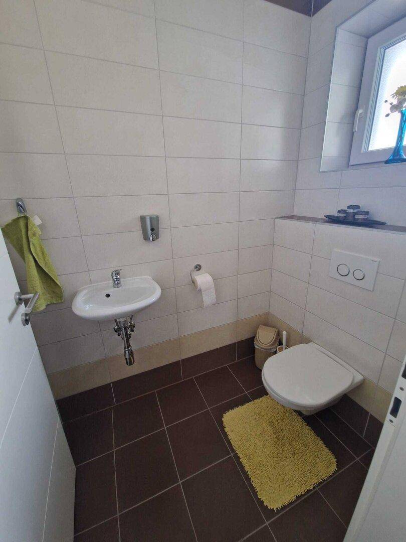 Helles Gäste-WC mit weißen und braunen Fliesen, wandhängendem WC und kleinem Waschbecken.