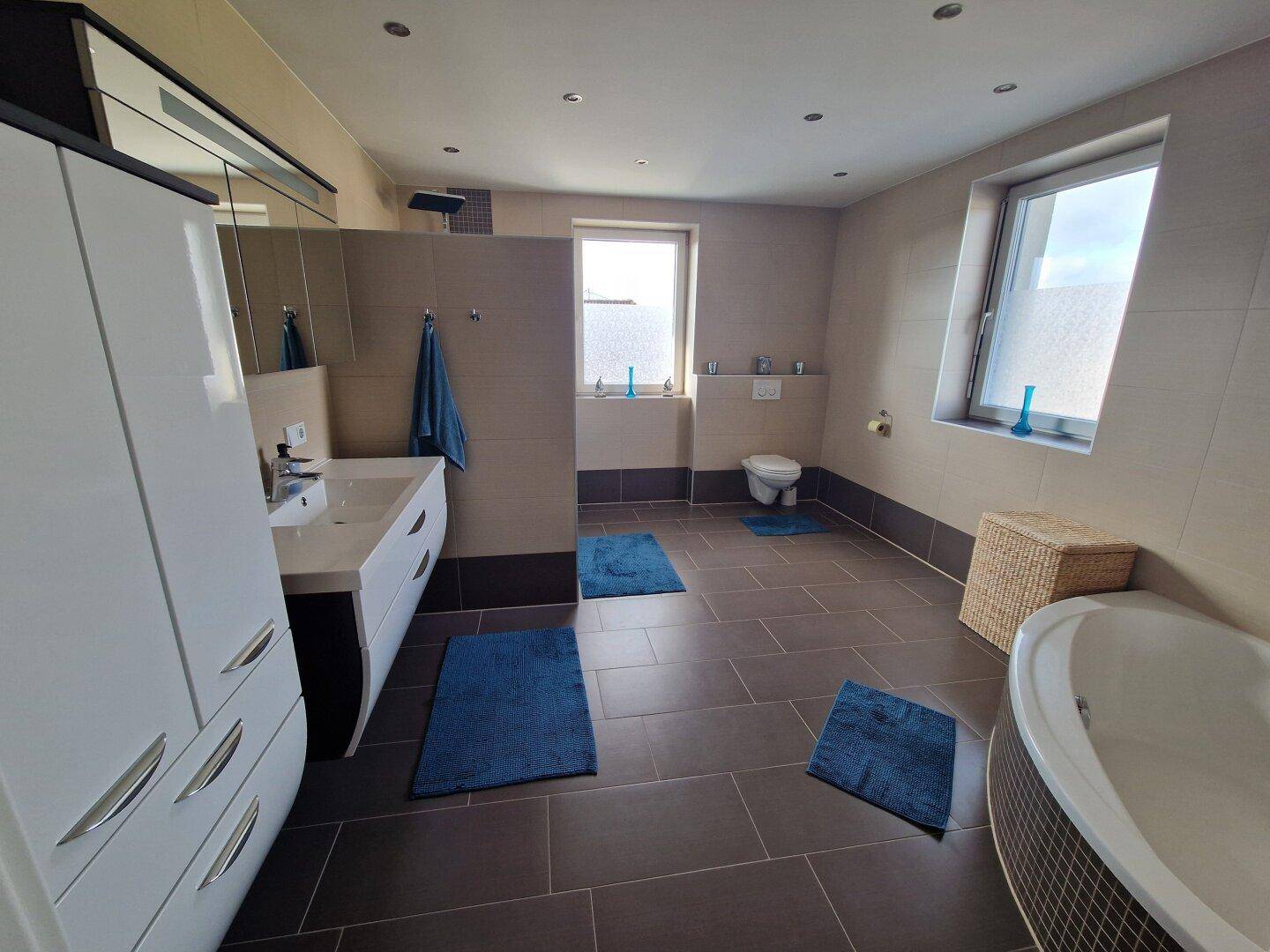 Modernes Badezimmer mit Eckbadewanne, Dusche, Doppelwaschbecken und Fenster für natürliches Licht.