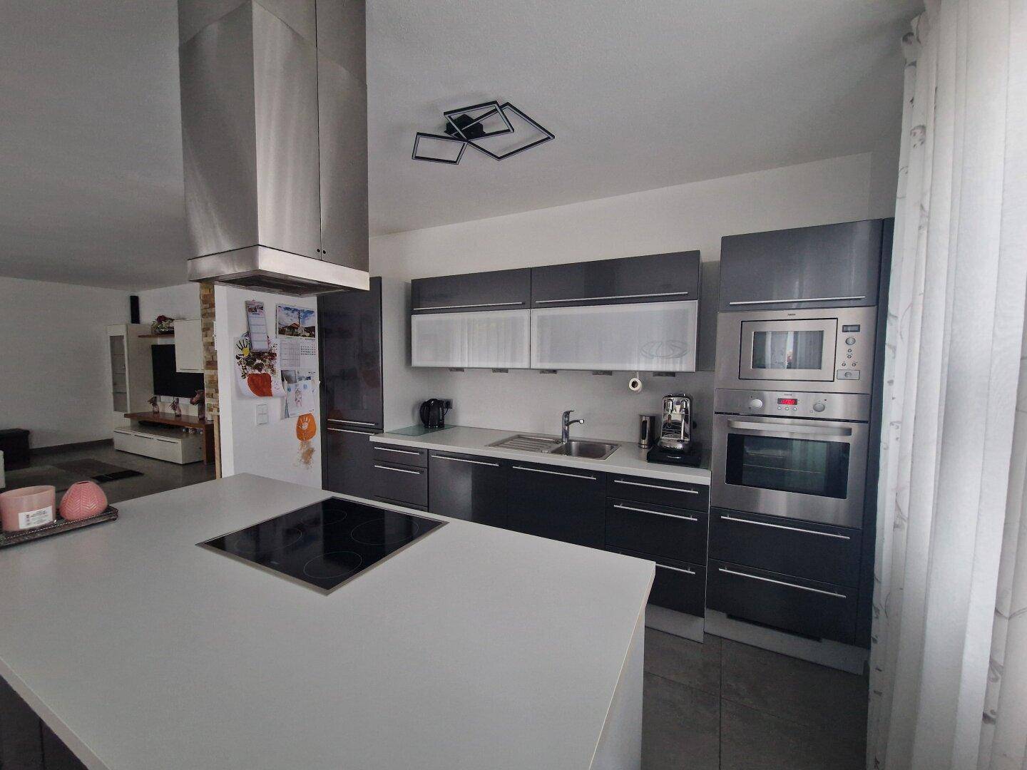 Moderne Küche mit Kochinsel, Induktionskochfeld, integrierten Geräten und Dunstabzugshaube.