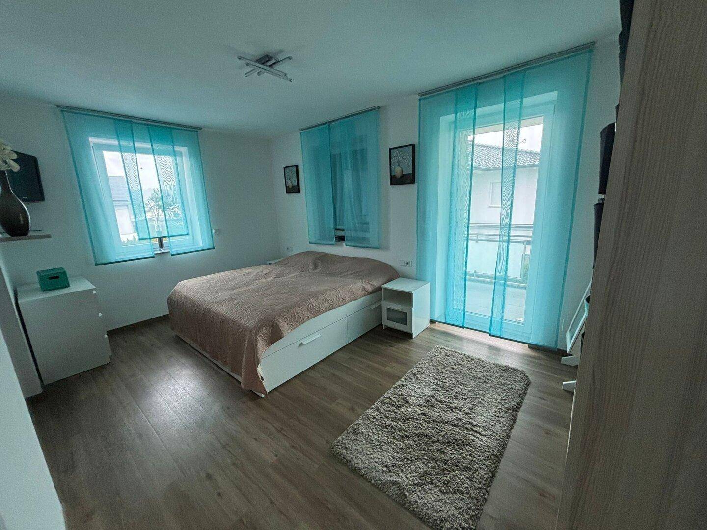 Helles Schlafzimmer mit Doppelbett, Holzfußboden und Zugang zum Balkon.