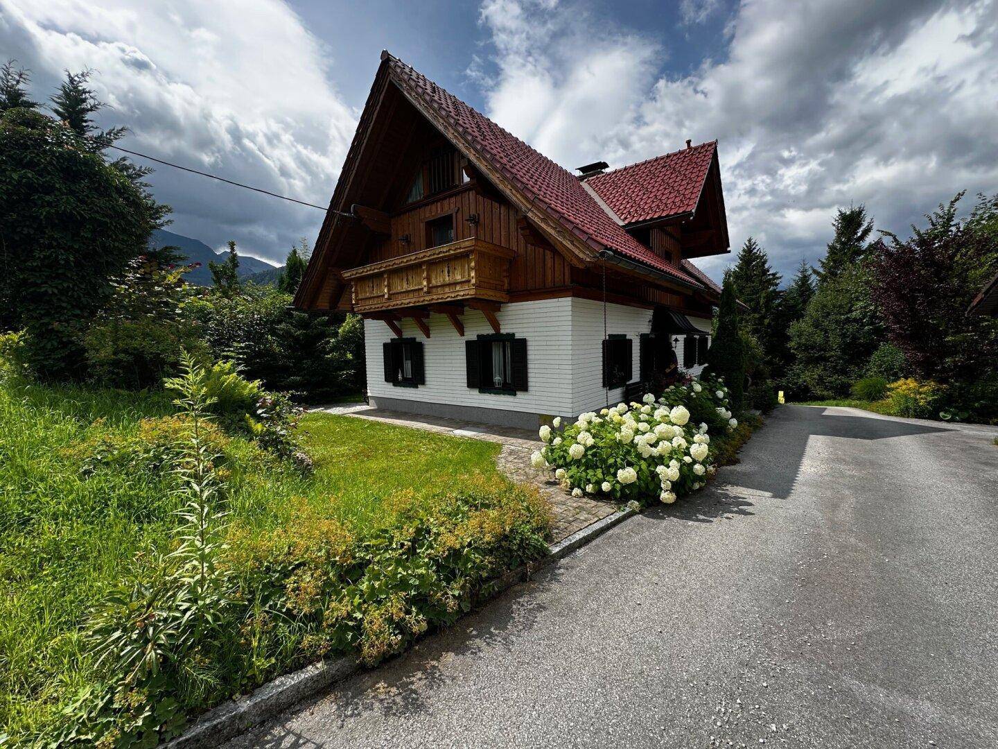 Charmantes Landhaus mit rotem Ziegeldach, umgeben von üppigem Grün und einer asphaltierten Auffahrt.