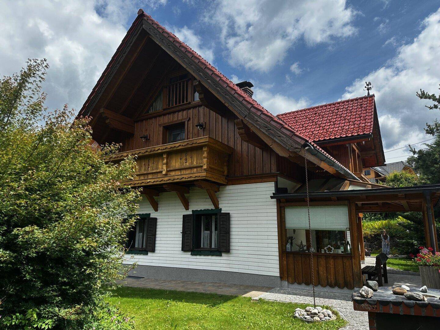 Seitlicher Blick auf das Haus mit überdachter Terrasse und traditionellen Holzelementen, umgeben von Grün.