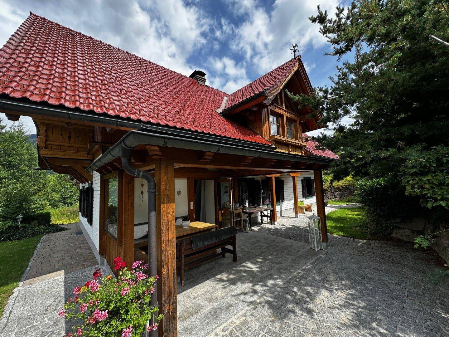 Überdachte Terrasse mit Holzbalken und gepflastertem Boden, ideal für Mahlzeiten im Freien am Haus.