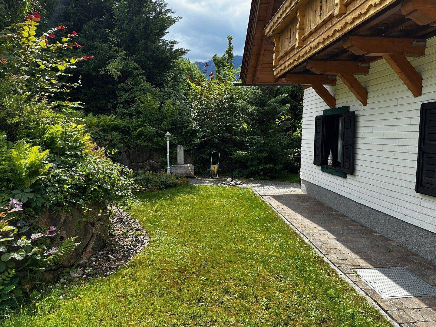 Gepflegter Rasenbereich mit üppiger Bepflanzung und einem Steinbeet neben dem traditionellen Haus.