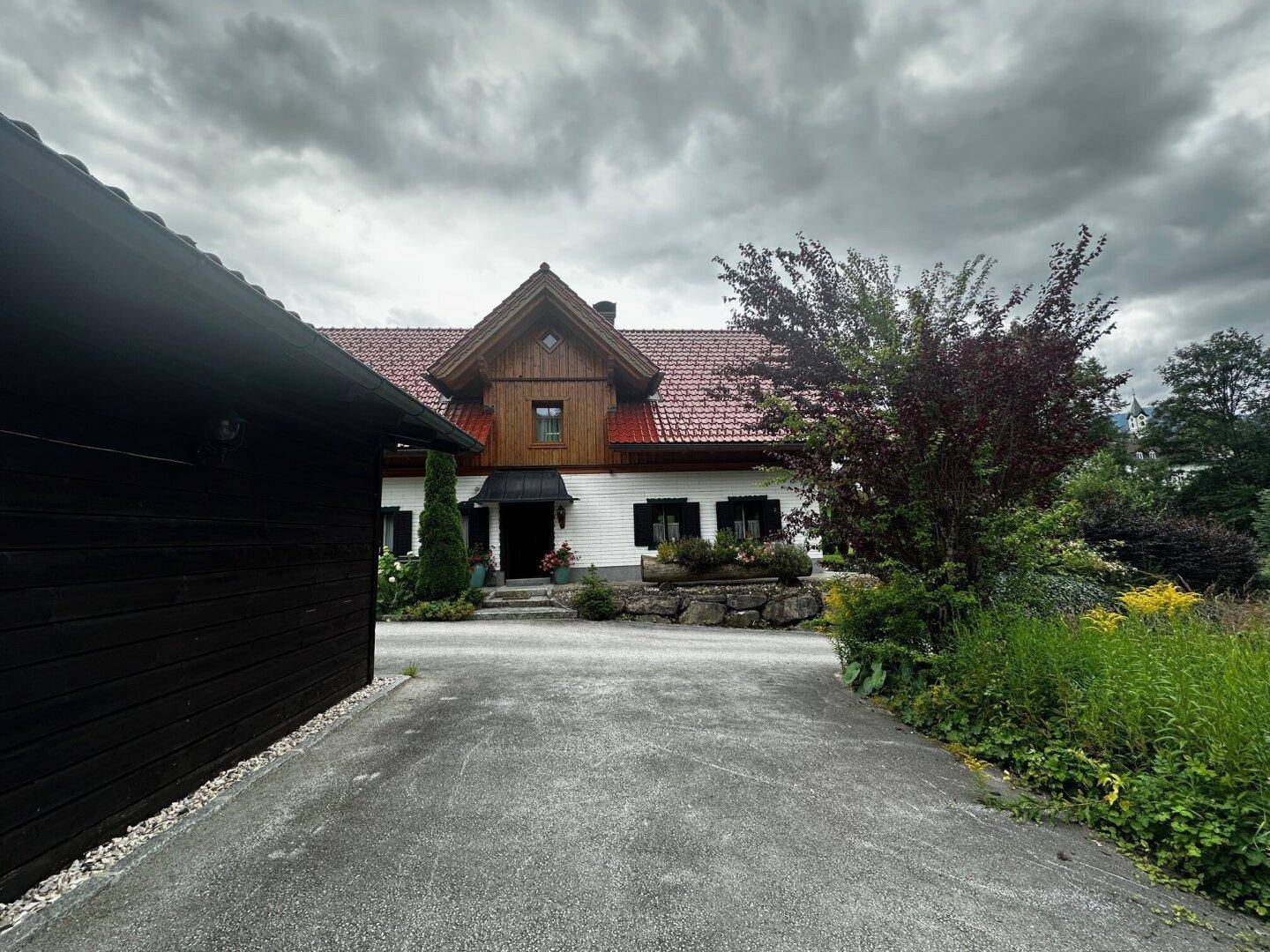 Frontansicht des traditionellen Hauses mit separatem Nebengebäude und langer Auffahrt.