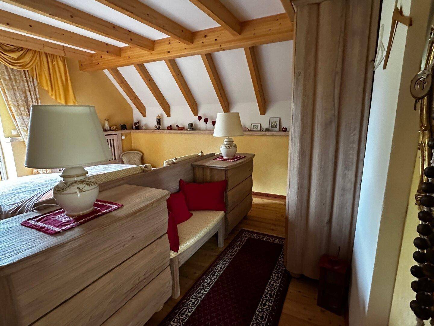 Schlafzimmer mit Holzbalkendecke, traditionellen Möbeln und warmen Farbtönen, mit Holzboden.