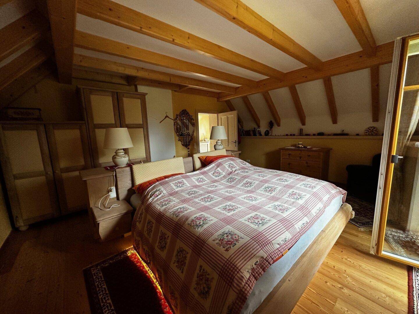 Helles Schlafzimmer mit Holzbalkendecke, Doppelbett und Zugang zu einem Balkon, mit Holzboden.