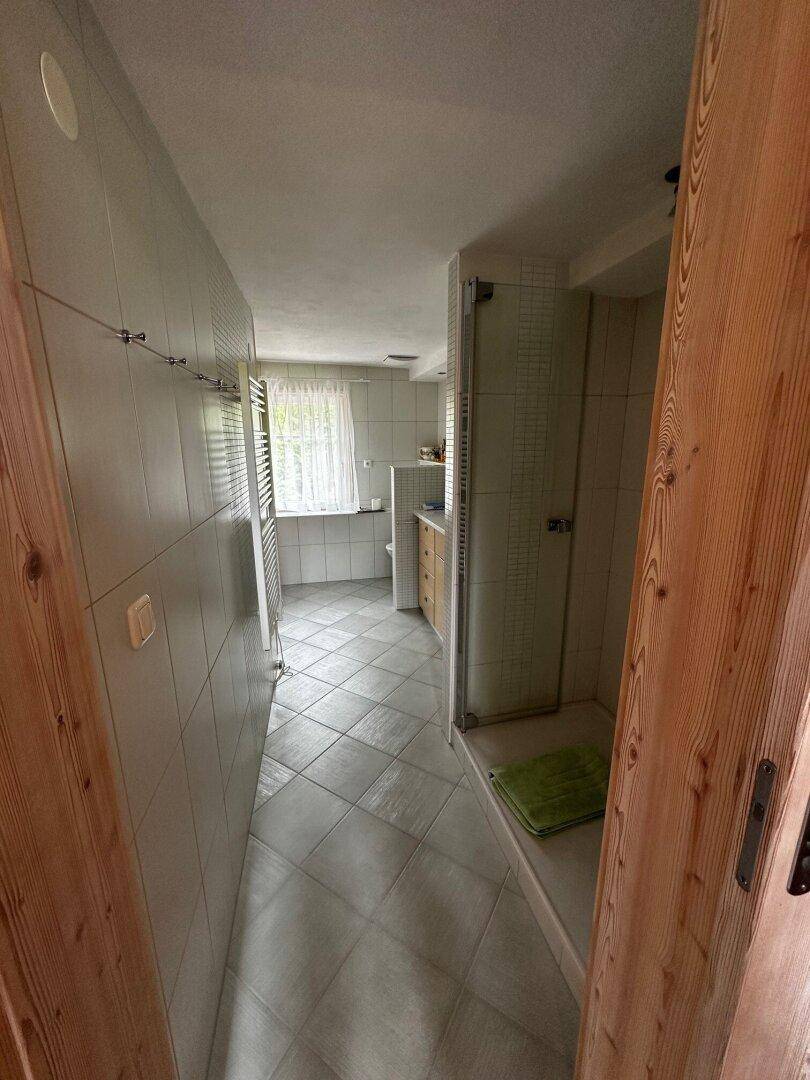 Modernes Badezimmer mit Fliesenboden, Duschbereich und Fenster für Tageslicht, mit Handtuchheizkörper.