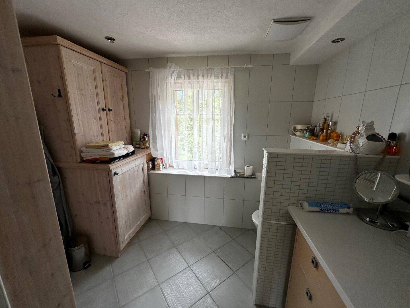 Helles Badezimmer mit Fenster, Fliesenboden und Holzschrank für Stauraum, mit Einzelwaschbecken.