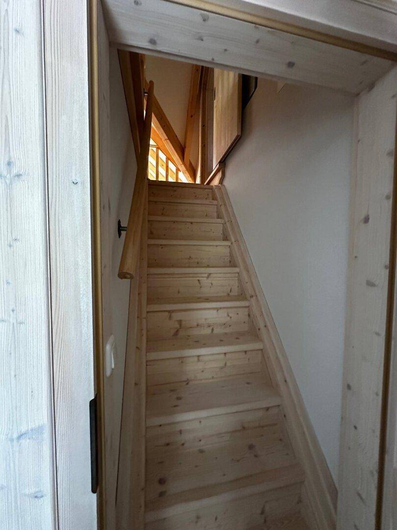 Holztreppe führt in die oberen Stockwerke, mit natürlichem Holzfinish und Geländer.