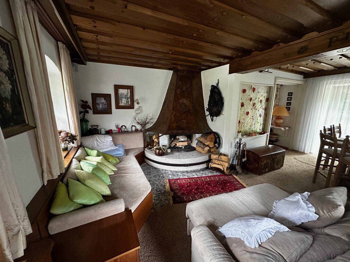 Gemütliches Wohnzimmer mit großem Kamin, Holzbalkendecke und Teppichboden, im alpinen Stil.
