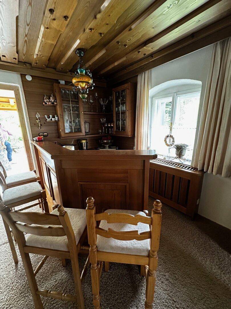 Gemütlicher Barbereich mit Holzeinrichtung, Holzbalkendecke und traditioneller Beleuchtung, mit Teppichboden.