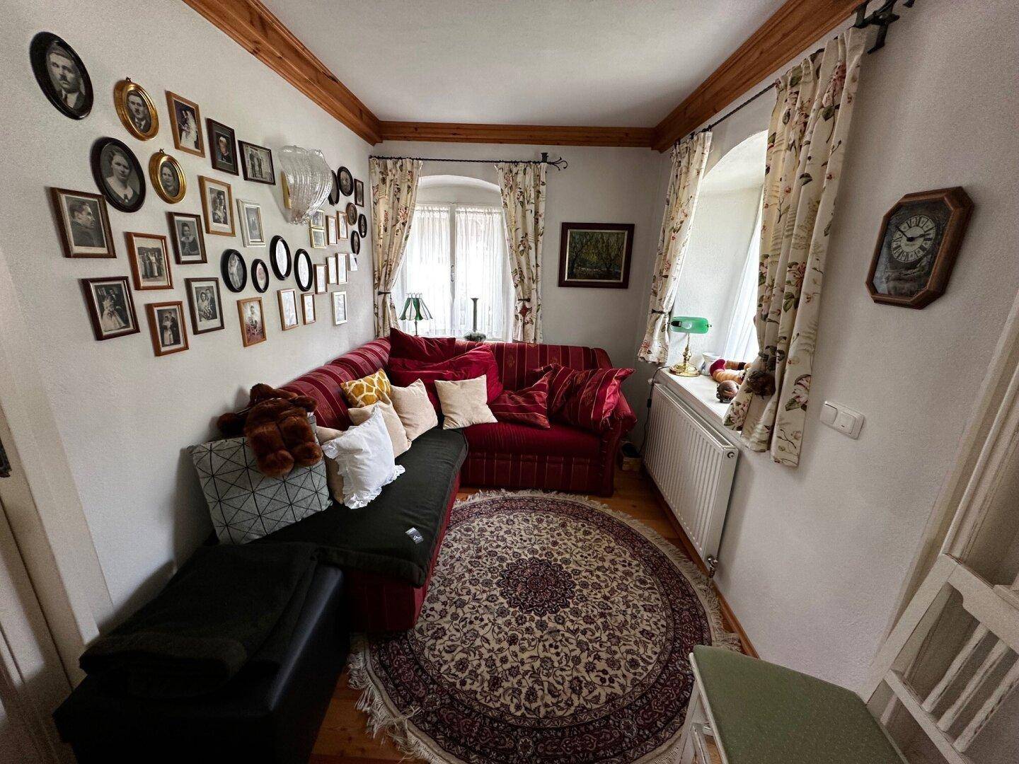 Gemütliches Wohnzimmer mit rotem Sofa, vielen Bildern an der Wand und traditionellem Teppich.