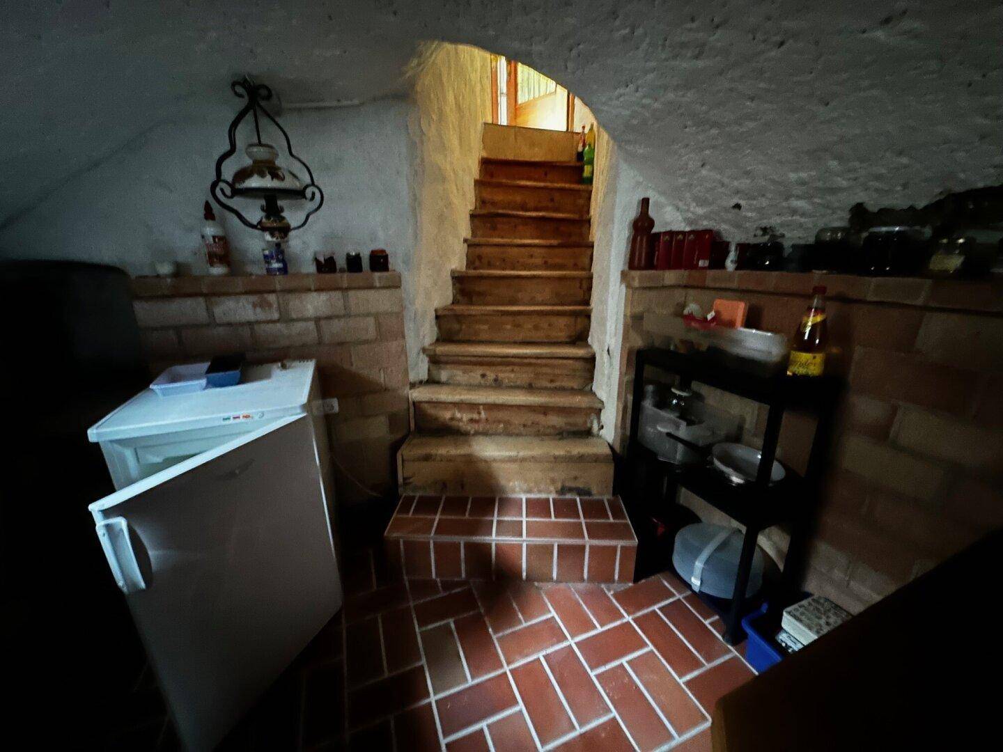 Gewölbekeller mit Holztreppe, Ziegelwänden und Stauraum, mit Terrakotta-Fliesenboden.