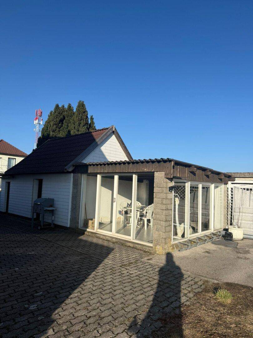 Anbau mit verglastem Wintergarten und gepflastertem Hofbereich neben dem Haus.