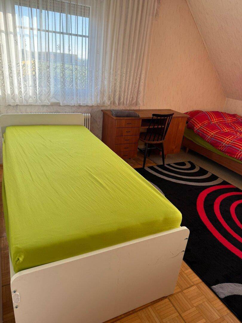Gemütliches Schlafzimmer mit zwei Betten, Holzboden und einem Fenster mit Vorhängen.