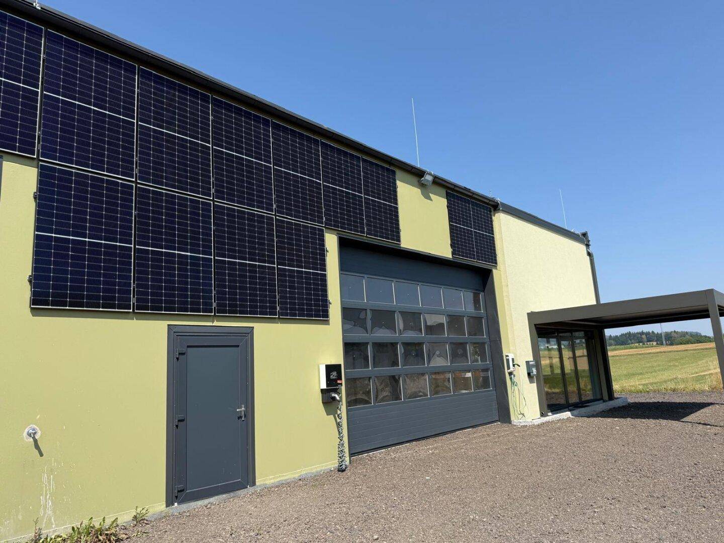 Gebäudeseite mit großem Garagentor, Photovoltaikmodulen und einem überdachten Eingangsbereich.