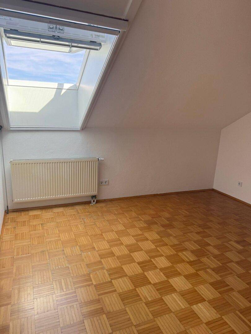 Helles Zimmer im Dachgeschoss mit Parkettboden, Dachfenster und schräger Decke.