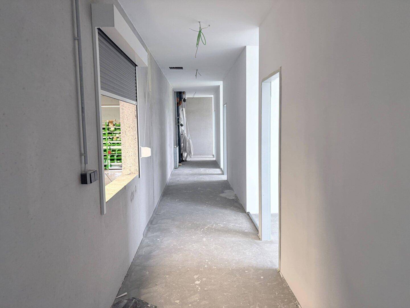 Langer, leerer Flur in einem Neubau mit einem Fenster und Rollladen.