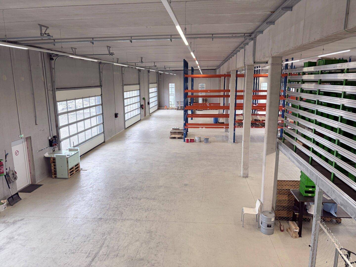 Geräumige Lagerhalle mit hohen Decken, Betonboden und mehreren Rolltoren, bereit zur Nutzung.