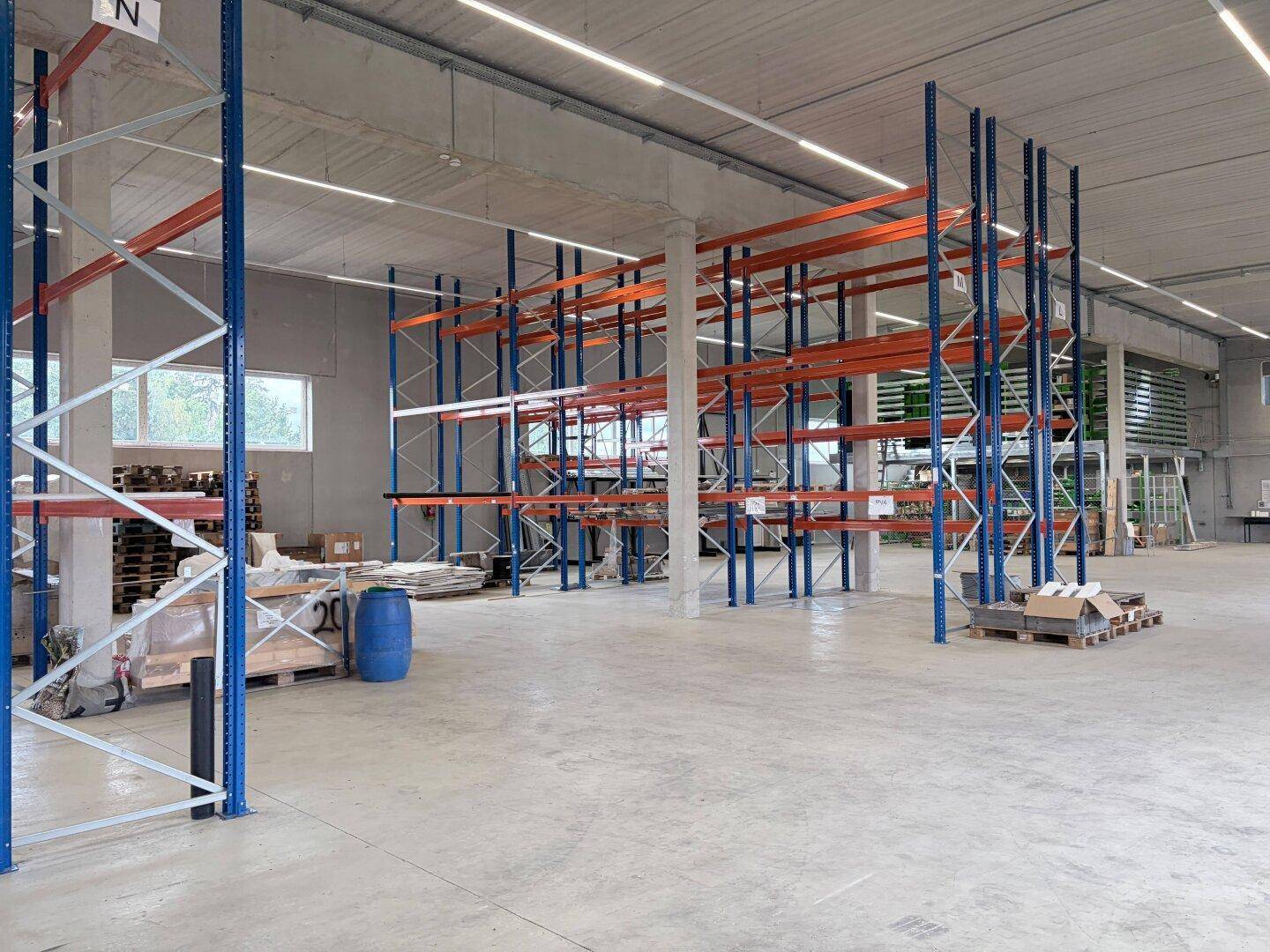 Weitläufige Lagerhalle mit hohen Decken, Betonboden und hohen Metallregalen, bereit zur Bestückung.