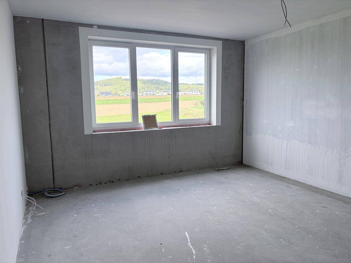 Unfertiger Raum mit großen Fenstern, die einen weiten Blick auf die grüne Landschaft bieten.