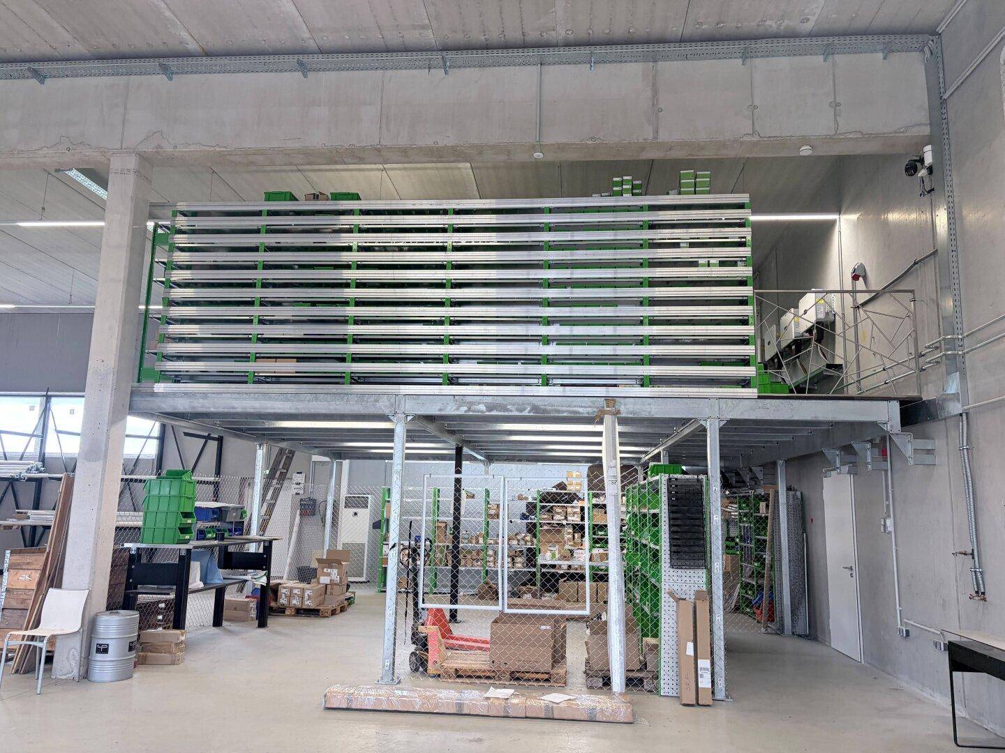 Zweistöckiges Lagersystem mit Metallregalen und einer Treppe in einer großen Halle.