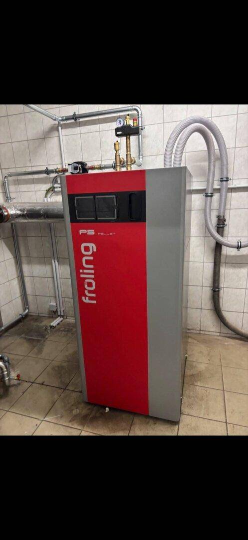 Moderner Froling Pelletkessel in einem gefliesten Heizraum mit sichtbaren Rohrleitungen.