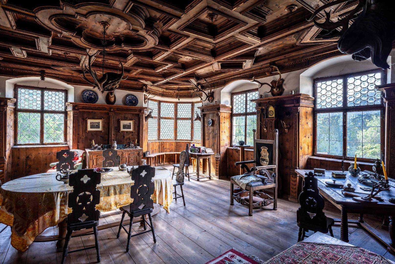 Prächtiger Speisesaal mit aufwendiger Holztäfelung, Kassettendecke und traditionellen Möbeln, hell erleuchtet.