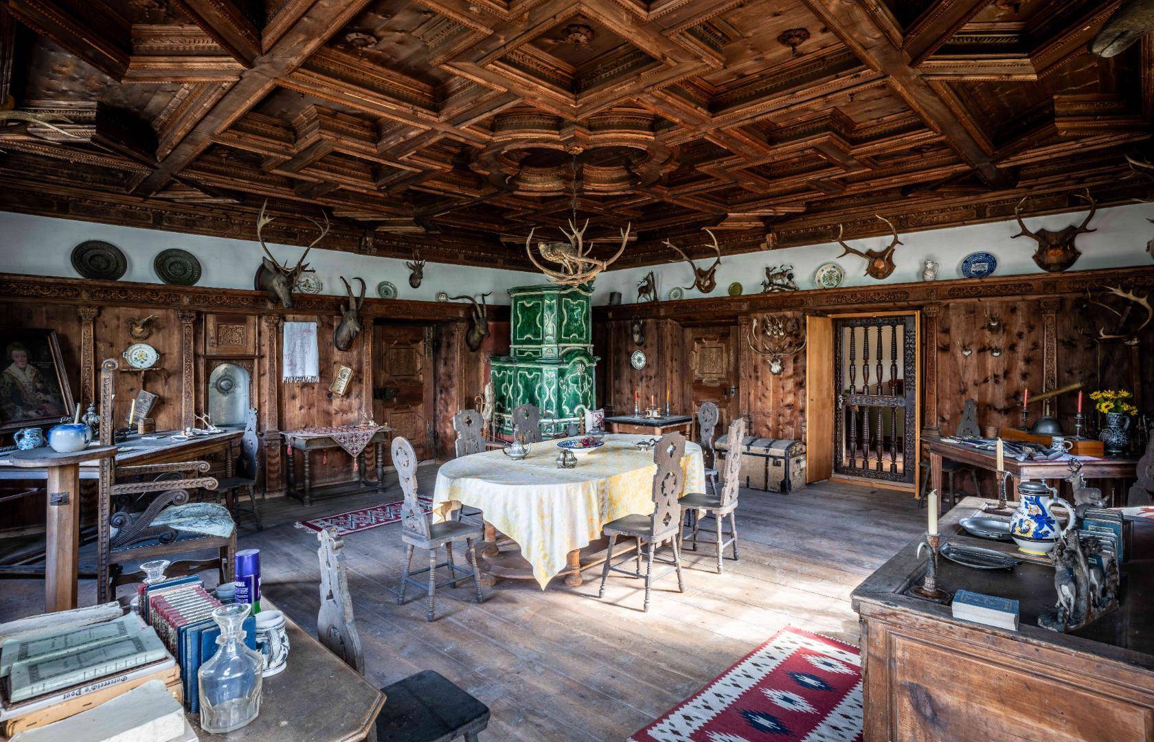 Historischer Speisesaal mit dunkler Holztäfelung, Kassettendecke und einem grünen Kachelofen als Blickfang.