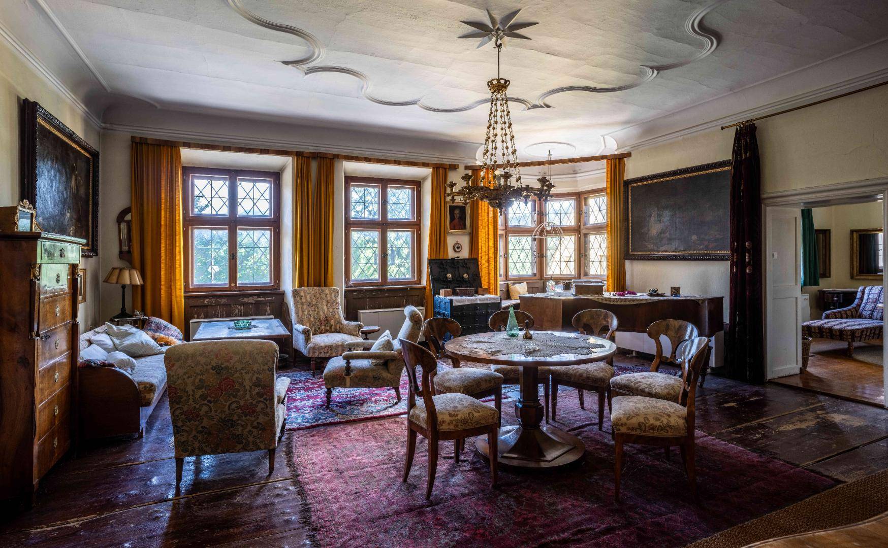 Elegantes Wohnzimmer mit Stuckdecke, Kronleuchter und antiken Möbeln, durch große Fenster hell beleuchtet.