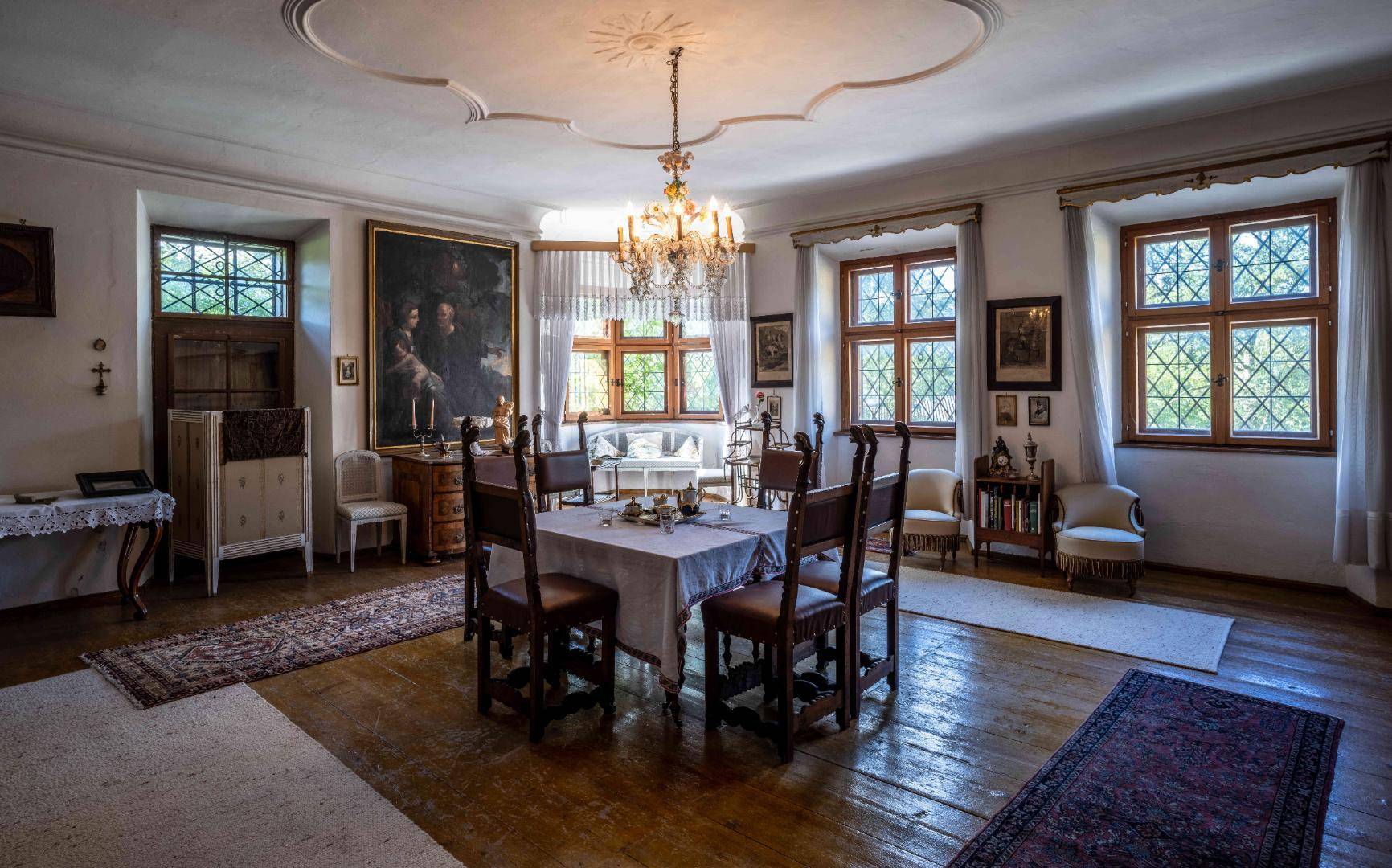 Heller Speisesaal mit elegantem Kronleuchter, Stuckdecke und traditionellen Möbeln, umgeben von Kunstwerken.