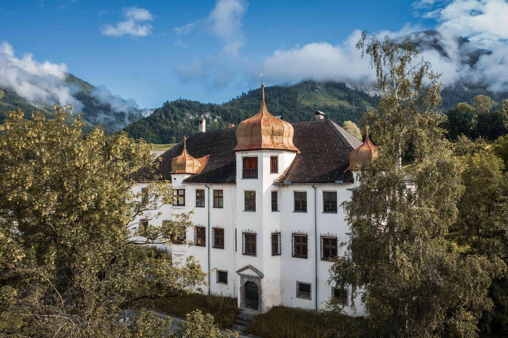 Majestätisches historisches Gebäude mit markanten Kupfertürmen und weißer Fassade vor einer Bergkulisse.