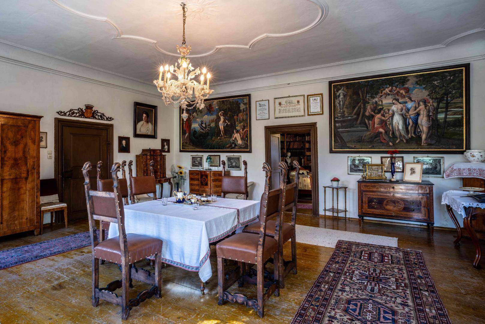 Geräumiger Speisesaal mit Holzboden, antiken Möbeln und zahlreichen Gemälden an den Wänden, klassisch eingerichtet.