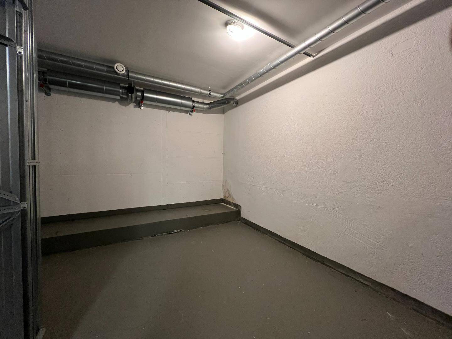 Kleiner Kellerraum mit sichtbaren Rohren an der Decke und einfacher Beleuchtung.