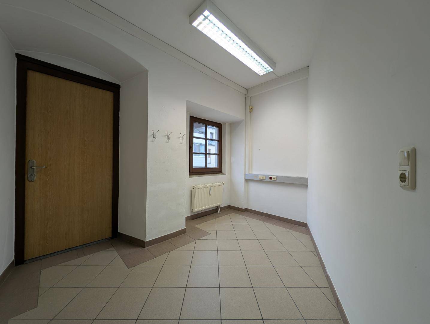 Kleiner, heller Eingangsbereich mit Fenster, Heizkörper und Garderobenhaken, ideal als Empfangsbereich.