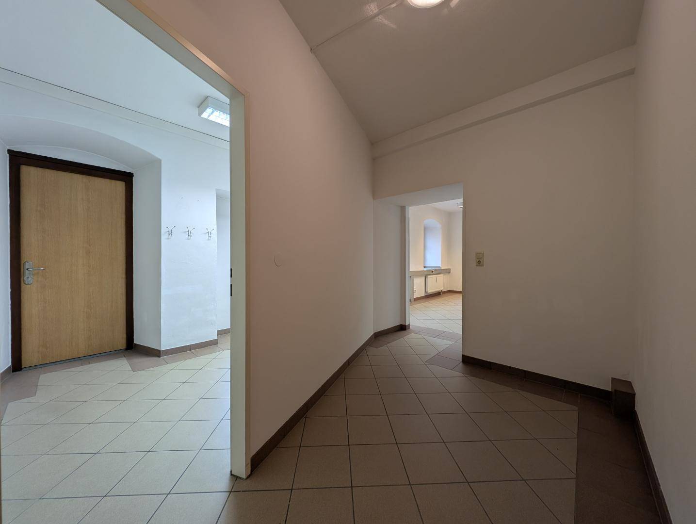 Schlichter Flur mit Fliesenboden und weißen Wänden, der zu weiteren Räumen im Gebäude führt.