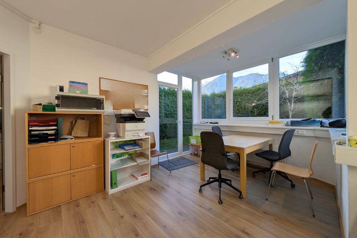 Helles Büro mit großen Fenstern, die einen Blick auf die Berge und viel Grün bieten, sowie einem Holzboden.