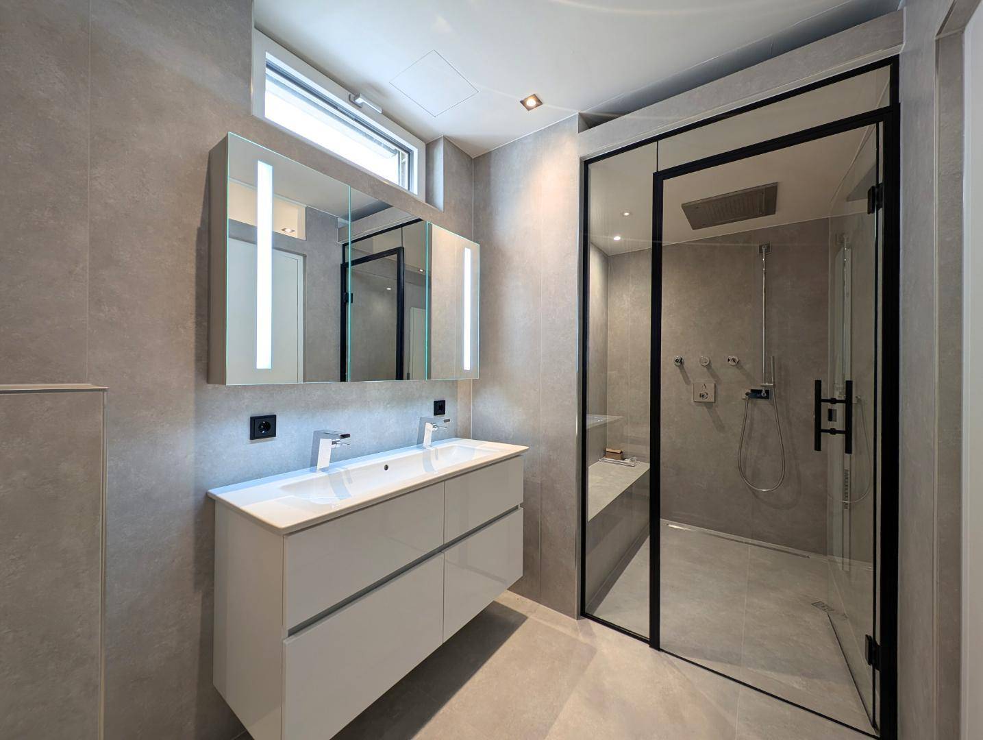 Modernes Badezimmer mit Doppelwaschbecken, großer Dusche und grauen Fliesen.