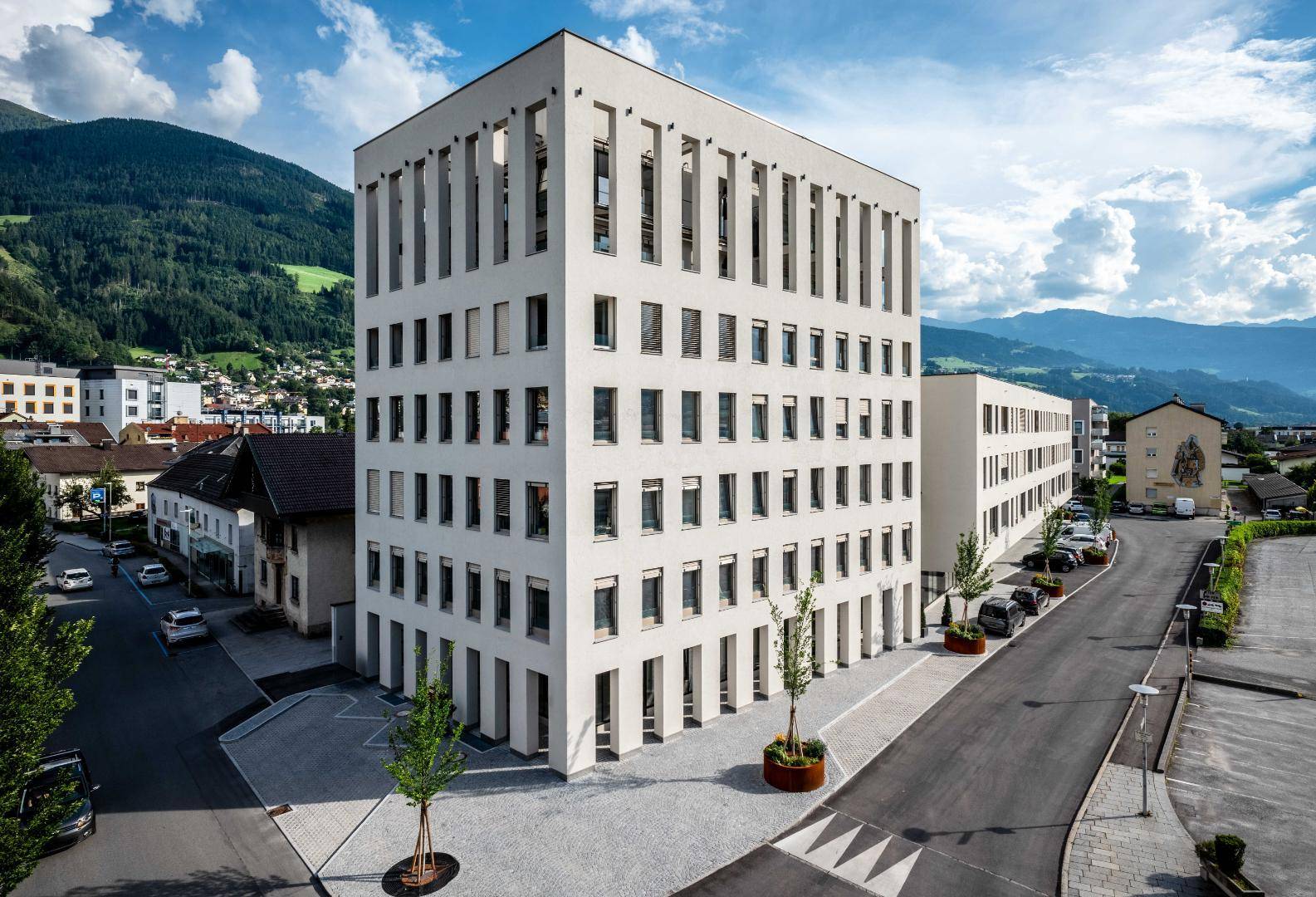 Modernes Wohngebäude mit klarer Architektur, vielen Fenstern und Bergblick im Hintergrund.