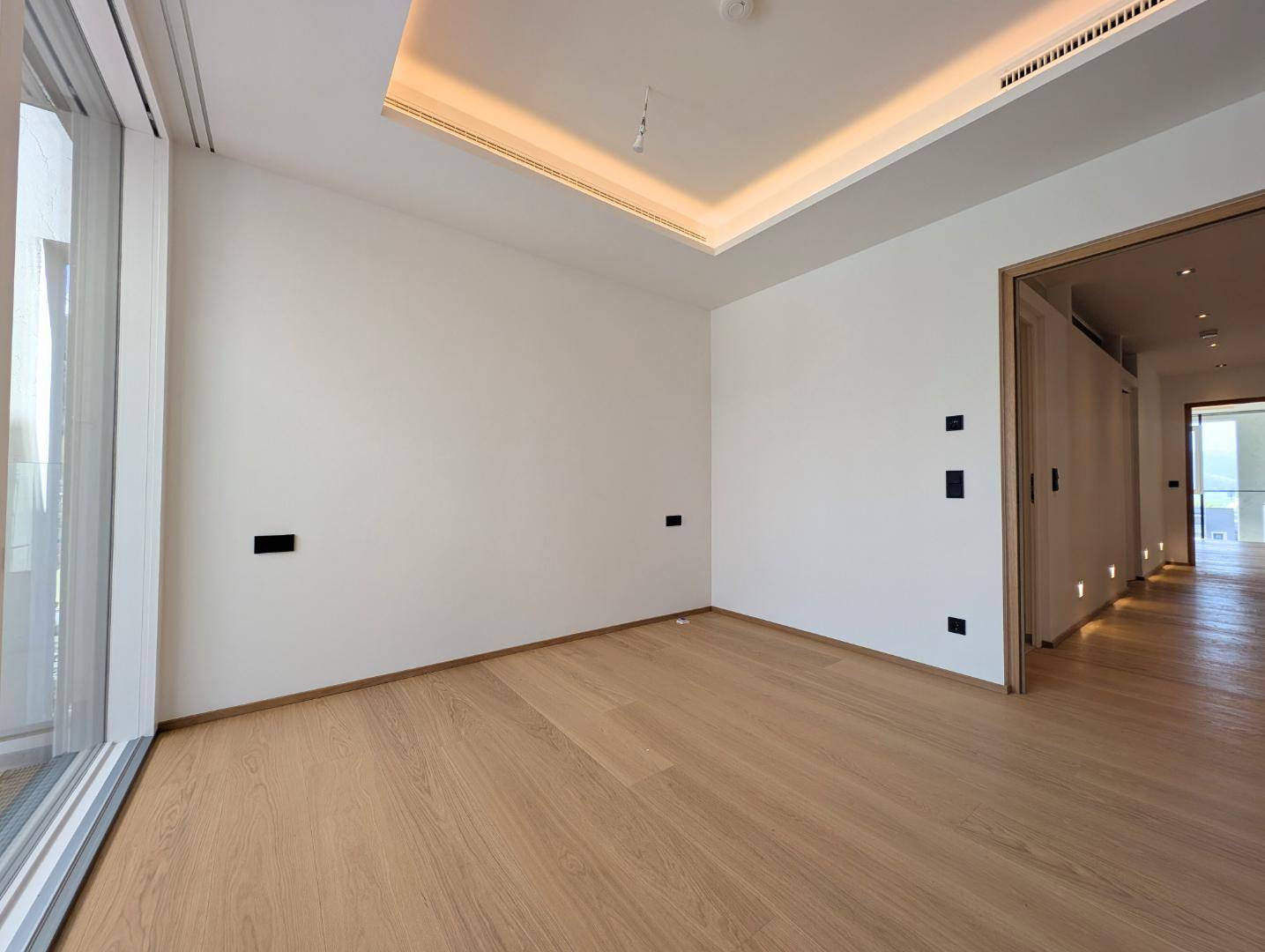 Leeres Schlafzimmer mit Holzboden und indirekter Deckenbeleuchtung.