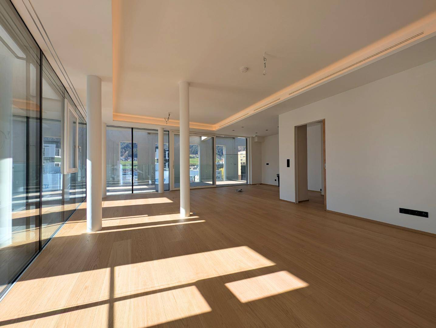Geräumiger, lichtdurchfluteter Wohnbereich mit Holzboden und modernen Säulen.